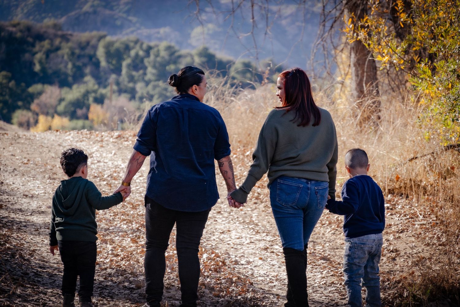 A silhouetted family holds hands while walking together on an autumn mountain trail at sunset.