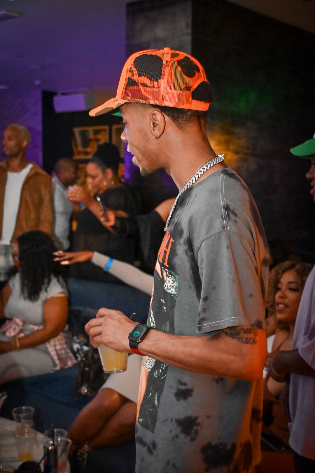 Person in orange baseball cap and gray t-shirt enjoying a lively nightclub atmosphere.