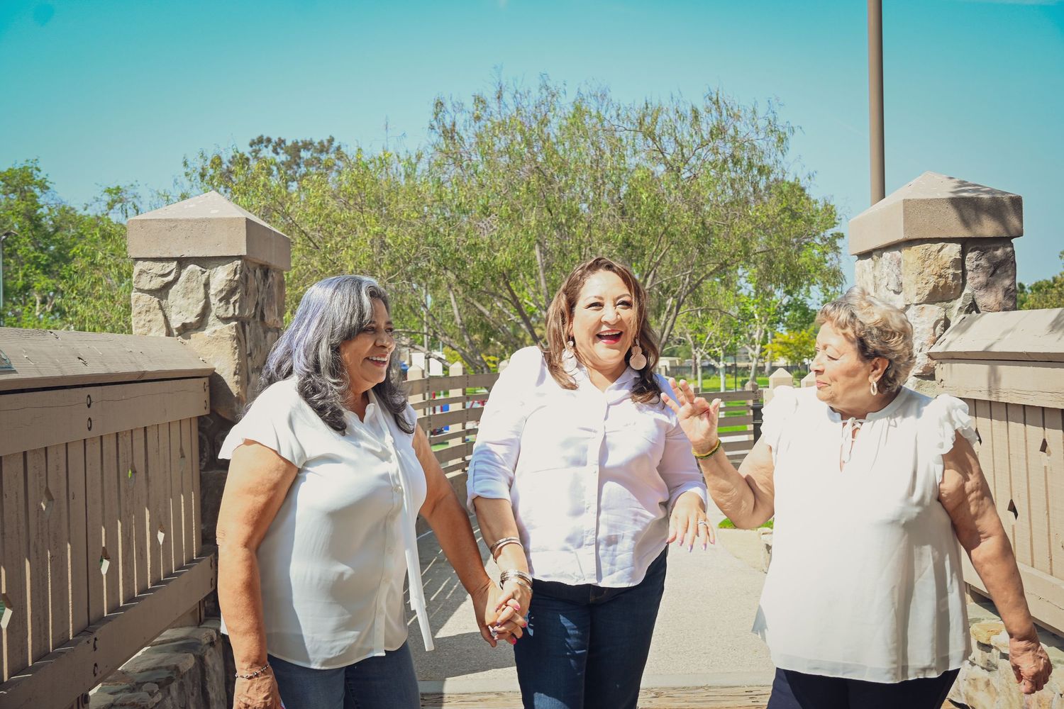 A group of people gather outdoors on a sunny day in a backyard setting with beige walls and greenery visible.