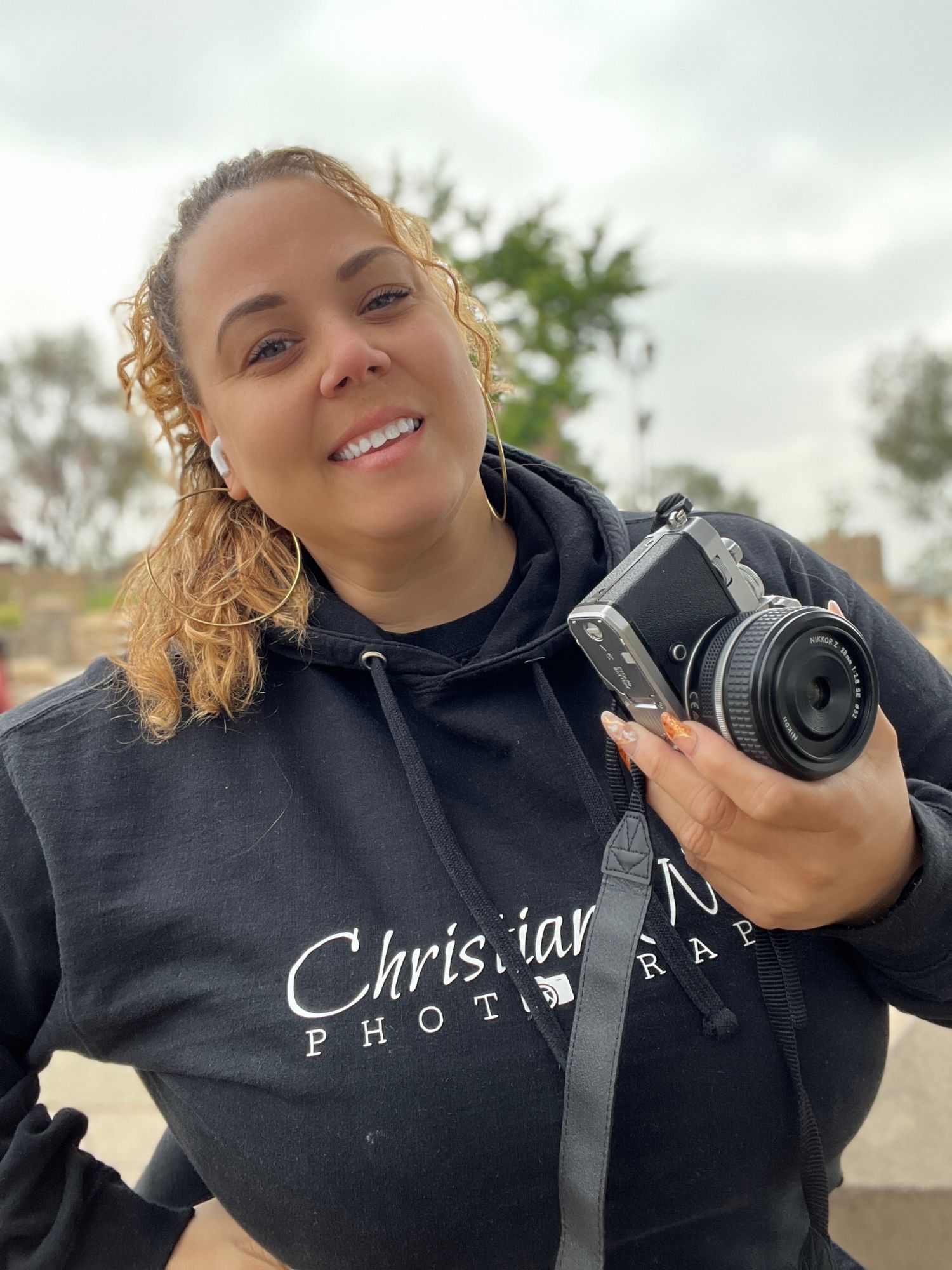 Photographer wearing black hoodie holding camera outdoors.