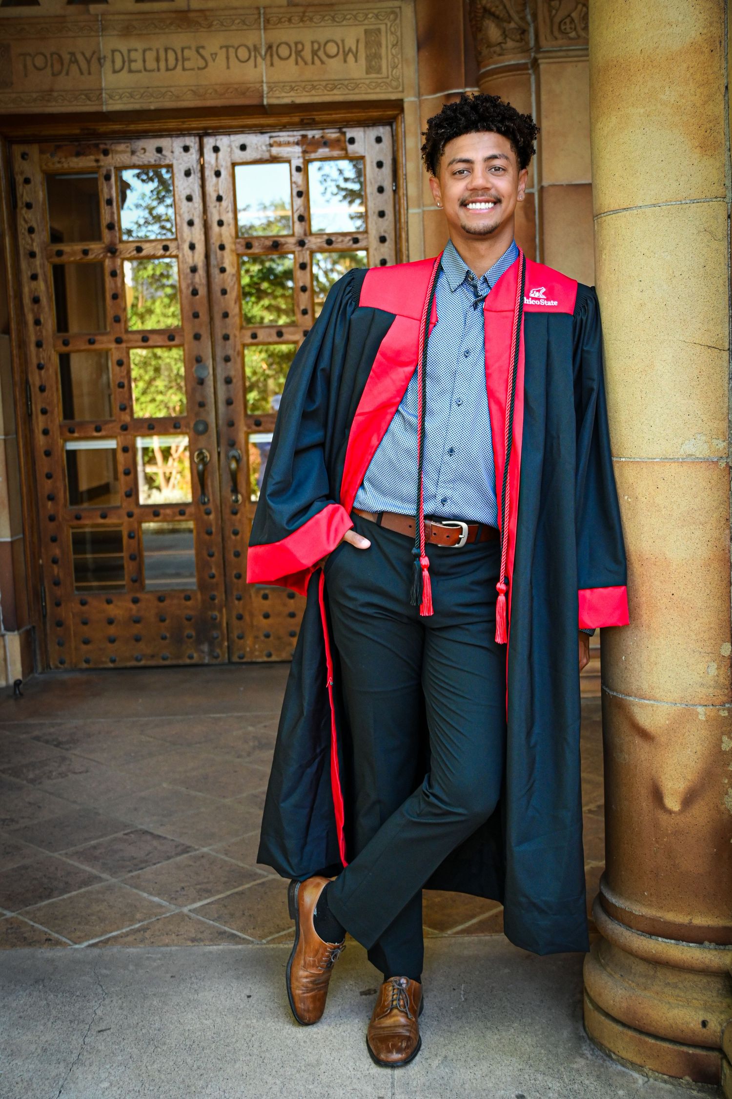 Graduate in academic regalia stands in front of decorative stone architecture during graduation photo session.