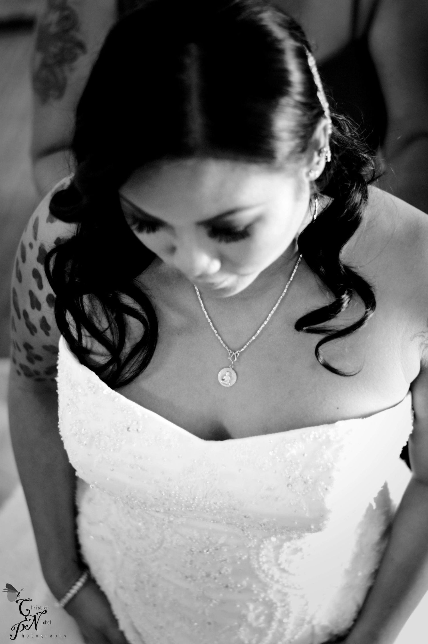 Black and white photo of a bride in a strapless lace gown wearing a delicate necklace, looking down elegantly.