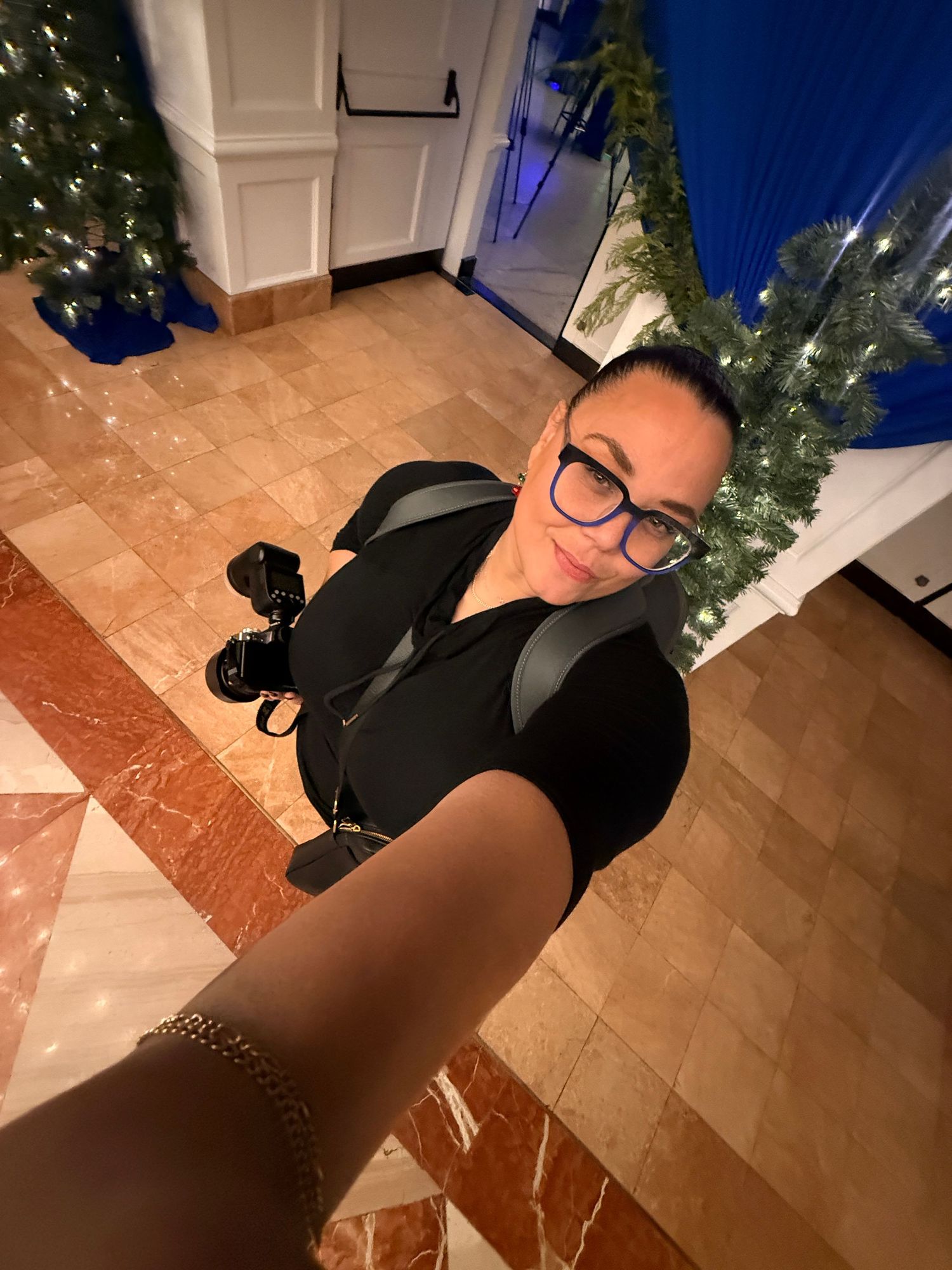 Photographer in black attire sitting on tiled floor with Christmas decorations in background.