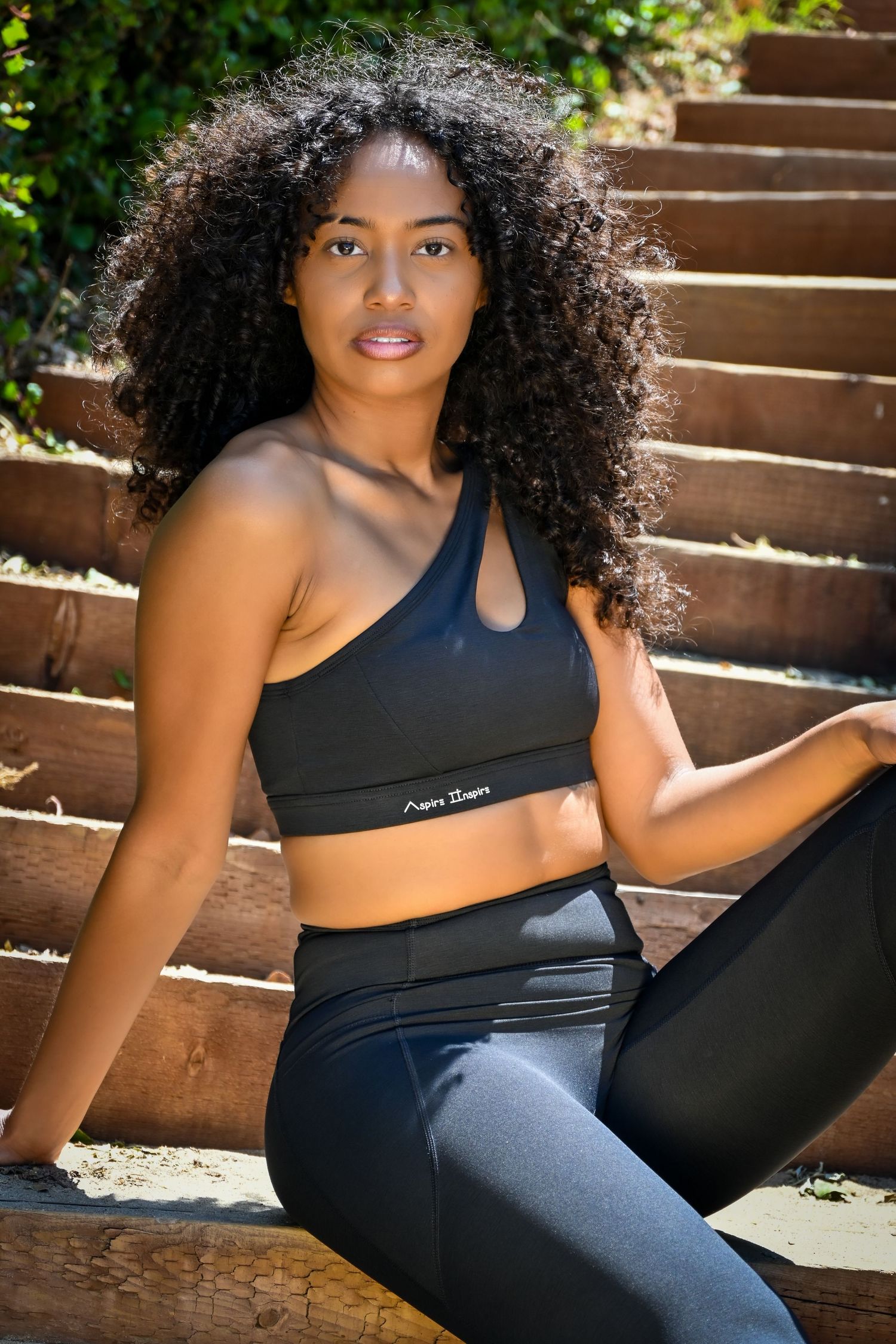 Athletic woman in black sportswear poses on outdoor steps during fitness photoshoot.