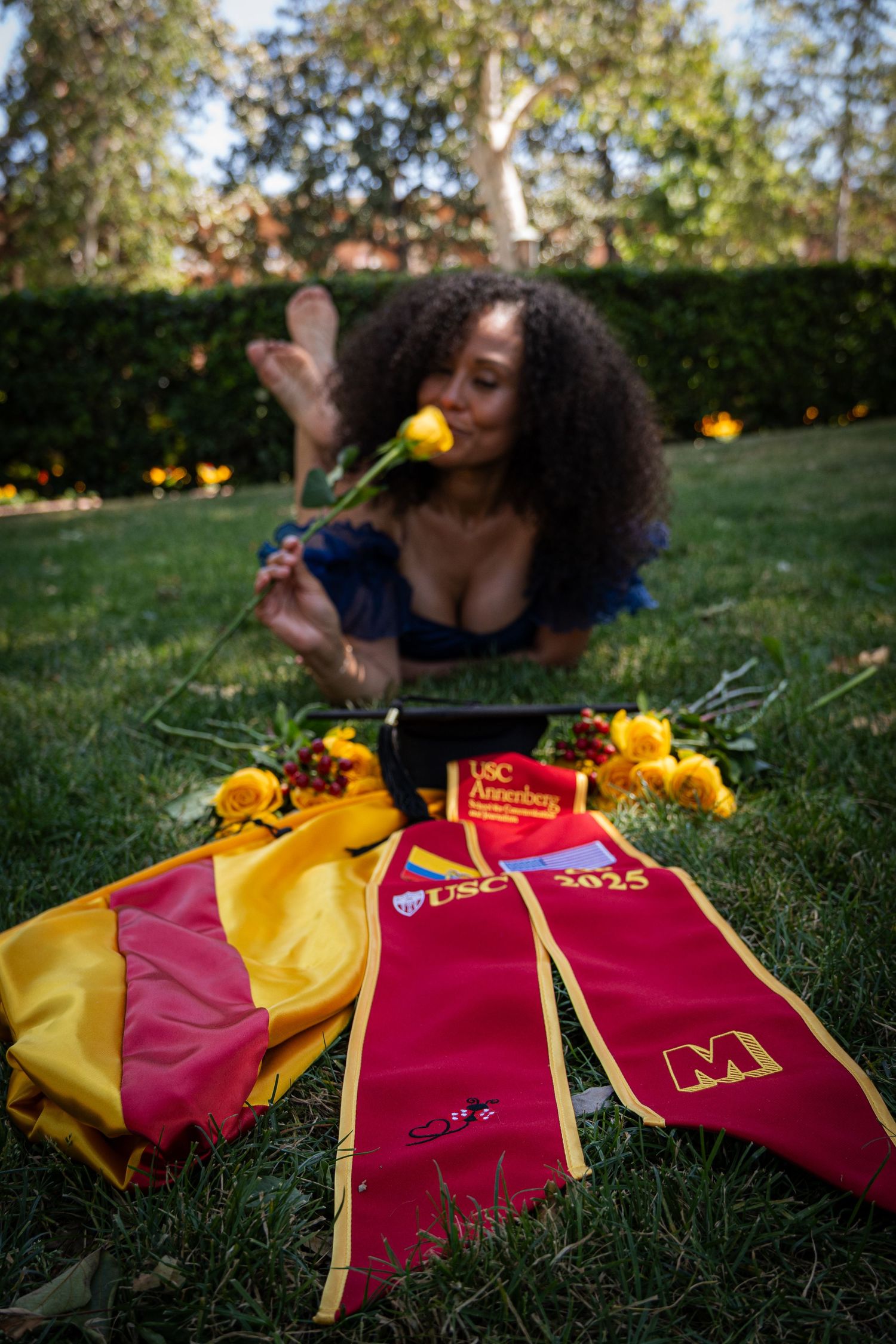 Red and gold graduation sashes laid out on grass with flowers.