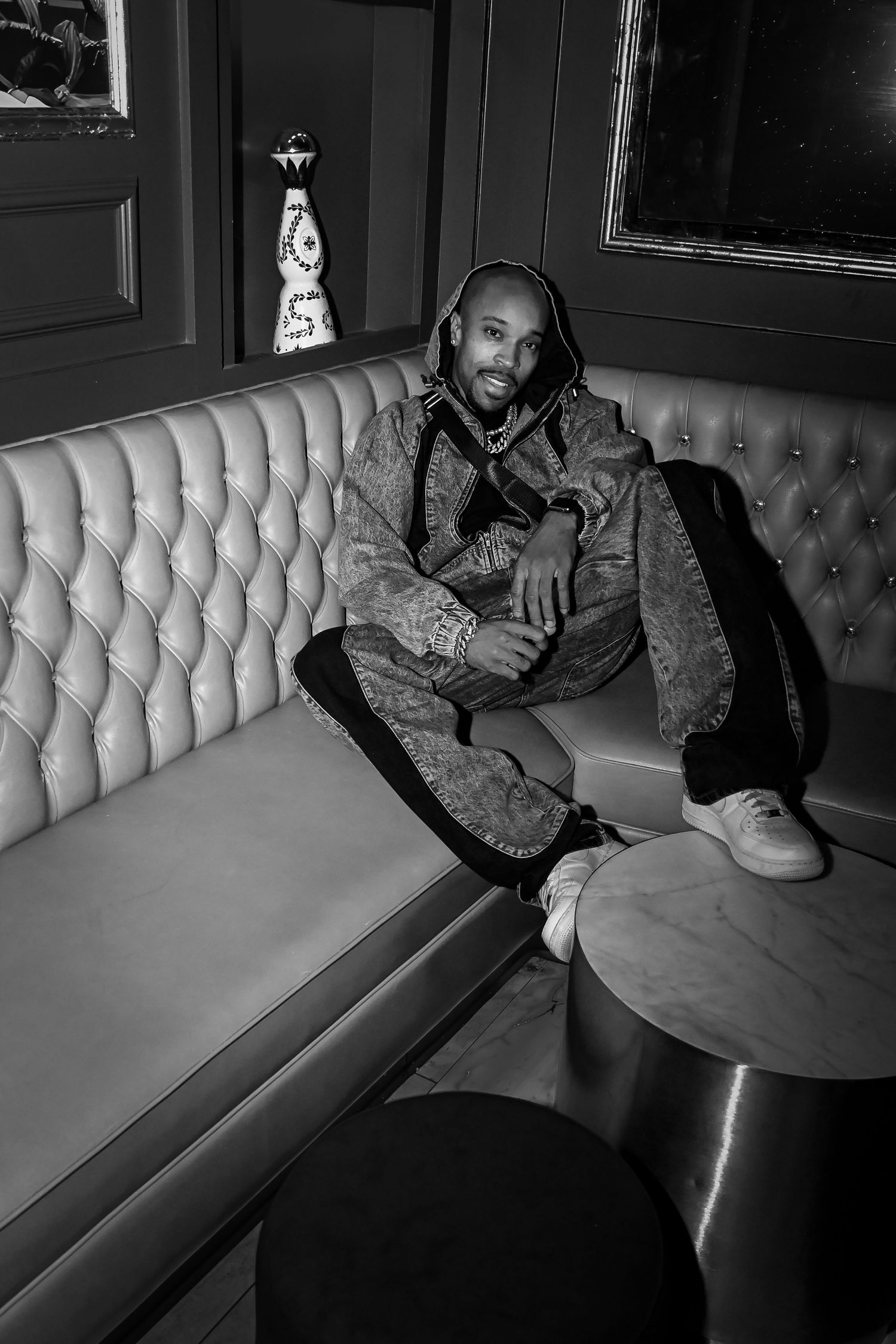 A series of black and white photos showing someone lounging on a curved white leather booth in a dimly lit setting.