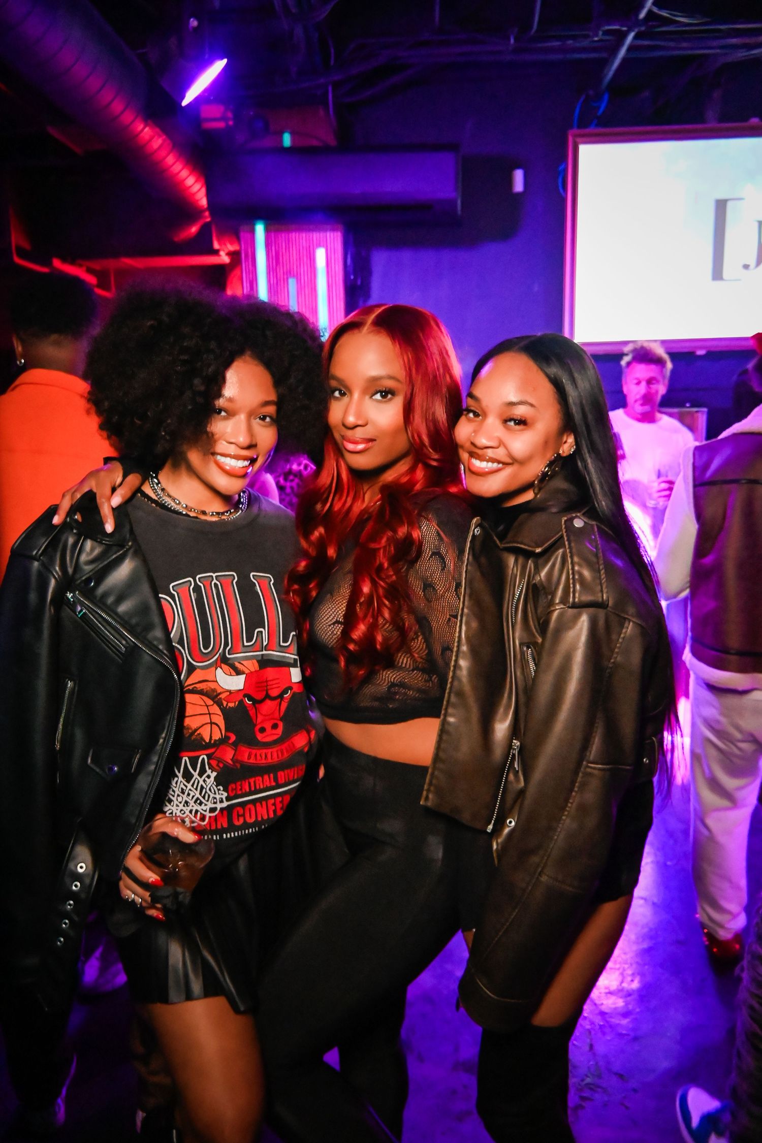 Friends enjoying a night out at a club with purple and red lighting in the background.