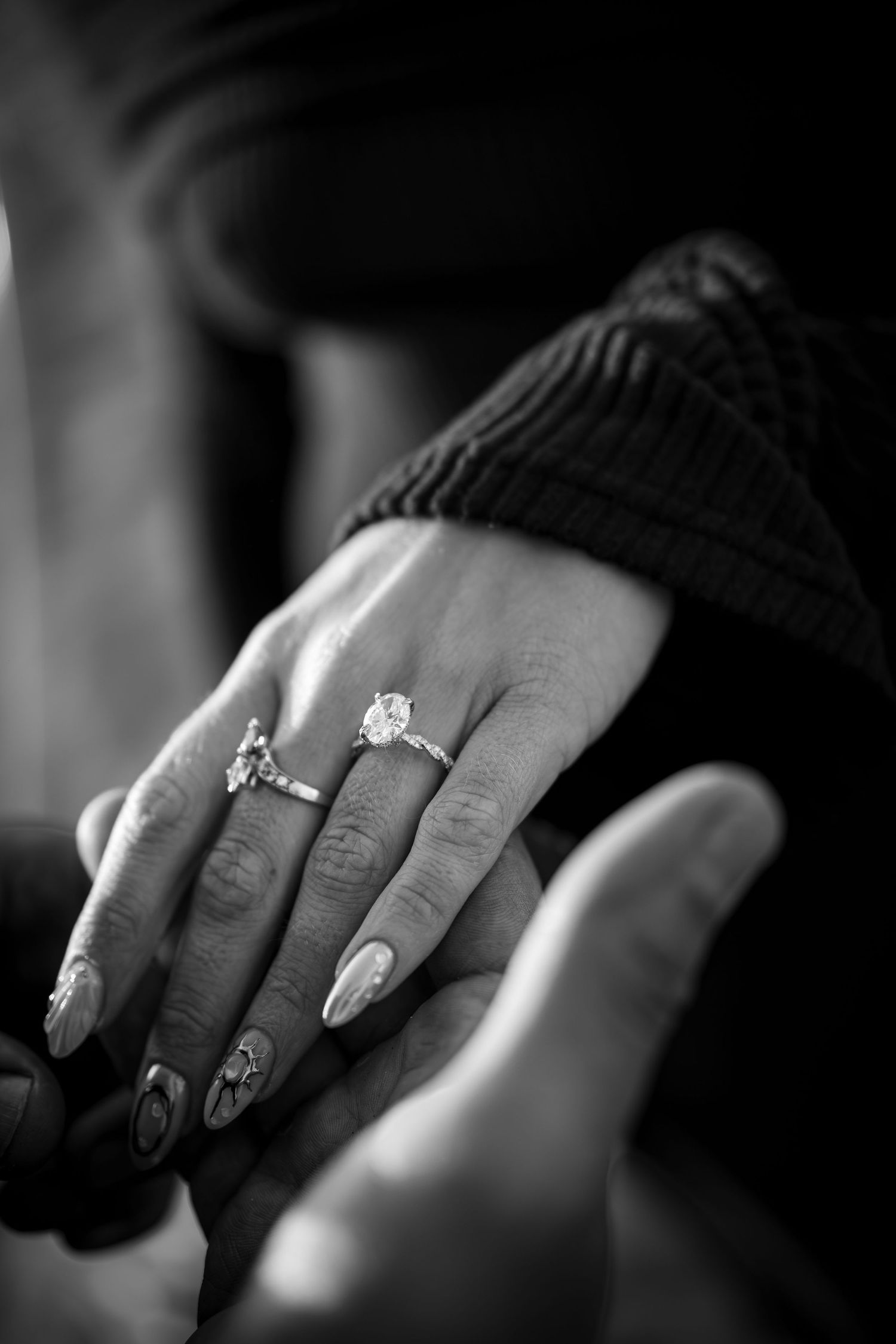 Black and white close-up of hands holding, featuring a sparkling diamond engagement ring on womans finger.