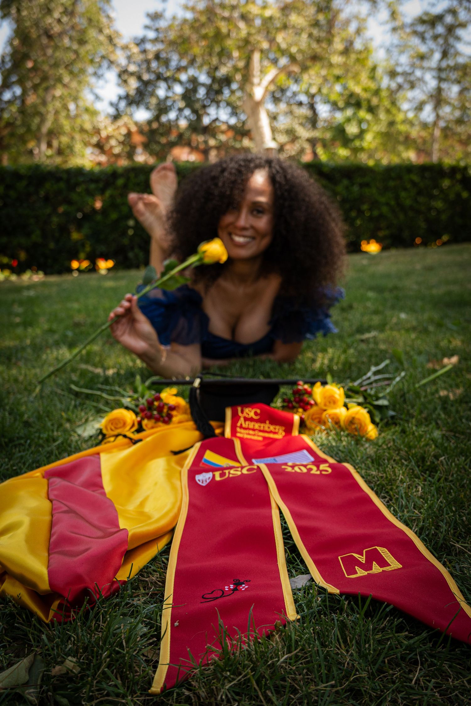 Graduation sashes and flowers arranged on grass in red and gold school colors.