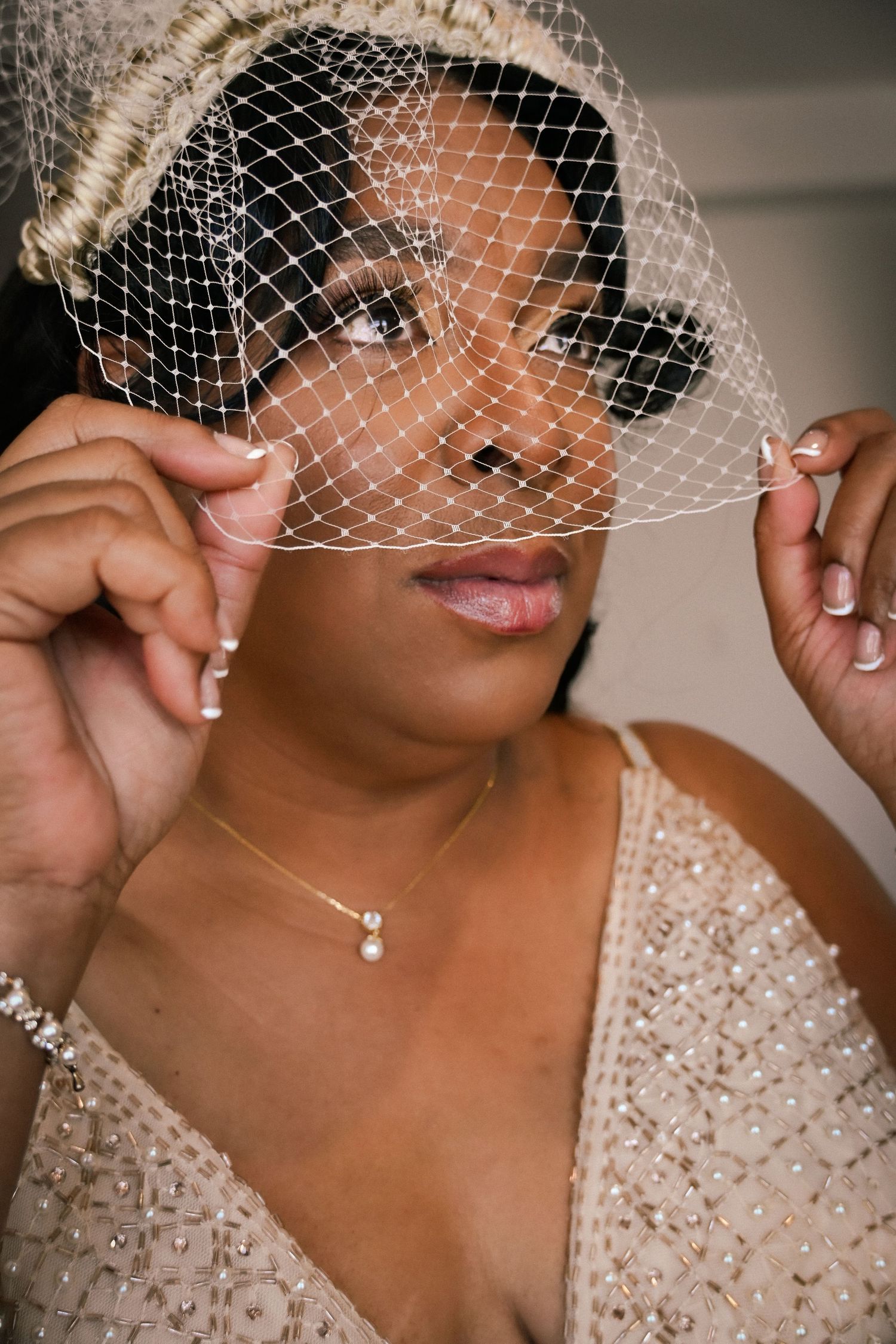 Bride wearing a birdcage veil and pearl necklace, adjusting her white net fascinator for her wedding day.