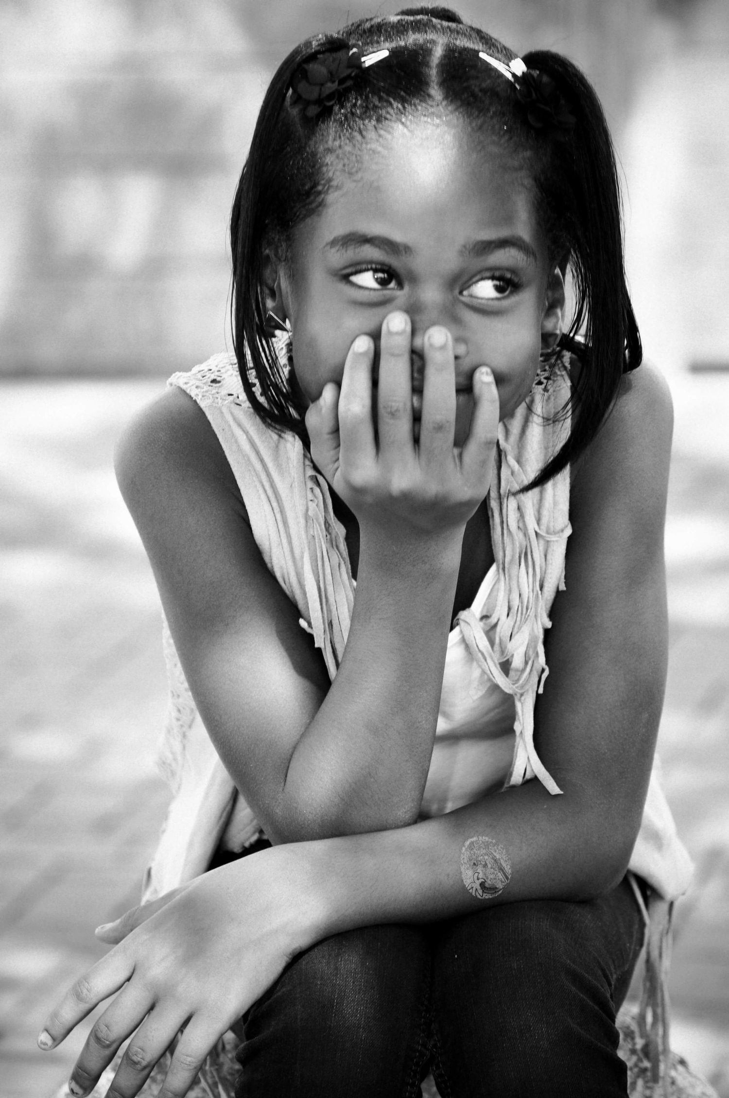 Black and white portrait of a young girl covering her mouth with her hand, smiling shyly while looking sideways.