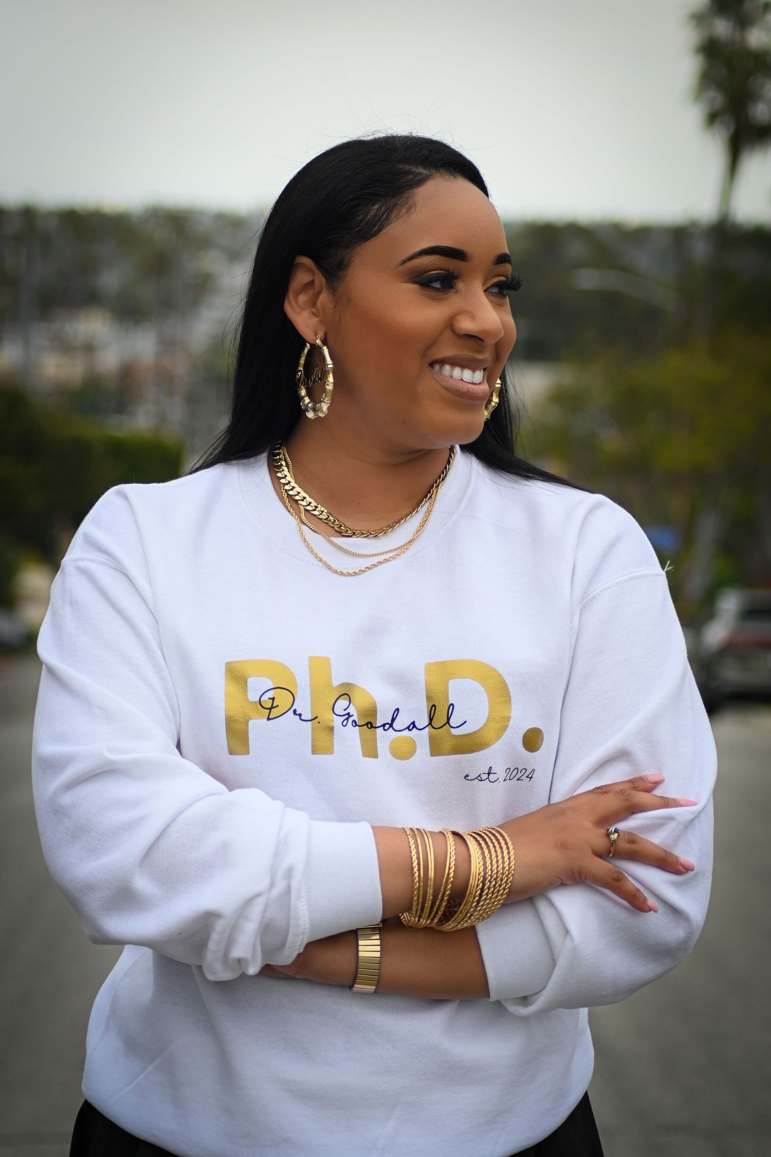 Confident pose in a white sweatshirt with gold Ph.D. lettering and matching accessories.