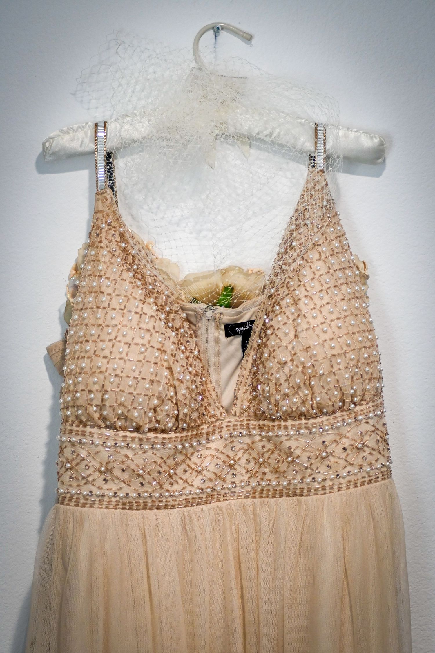 Elegant beige beaded evening gown with crystal embellishments and chiffon skirt on decorative hanger.