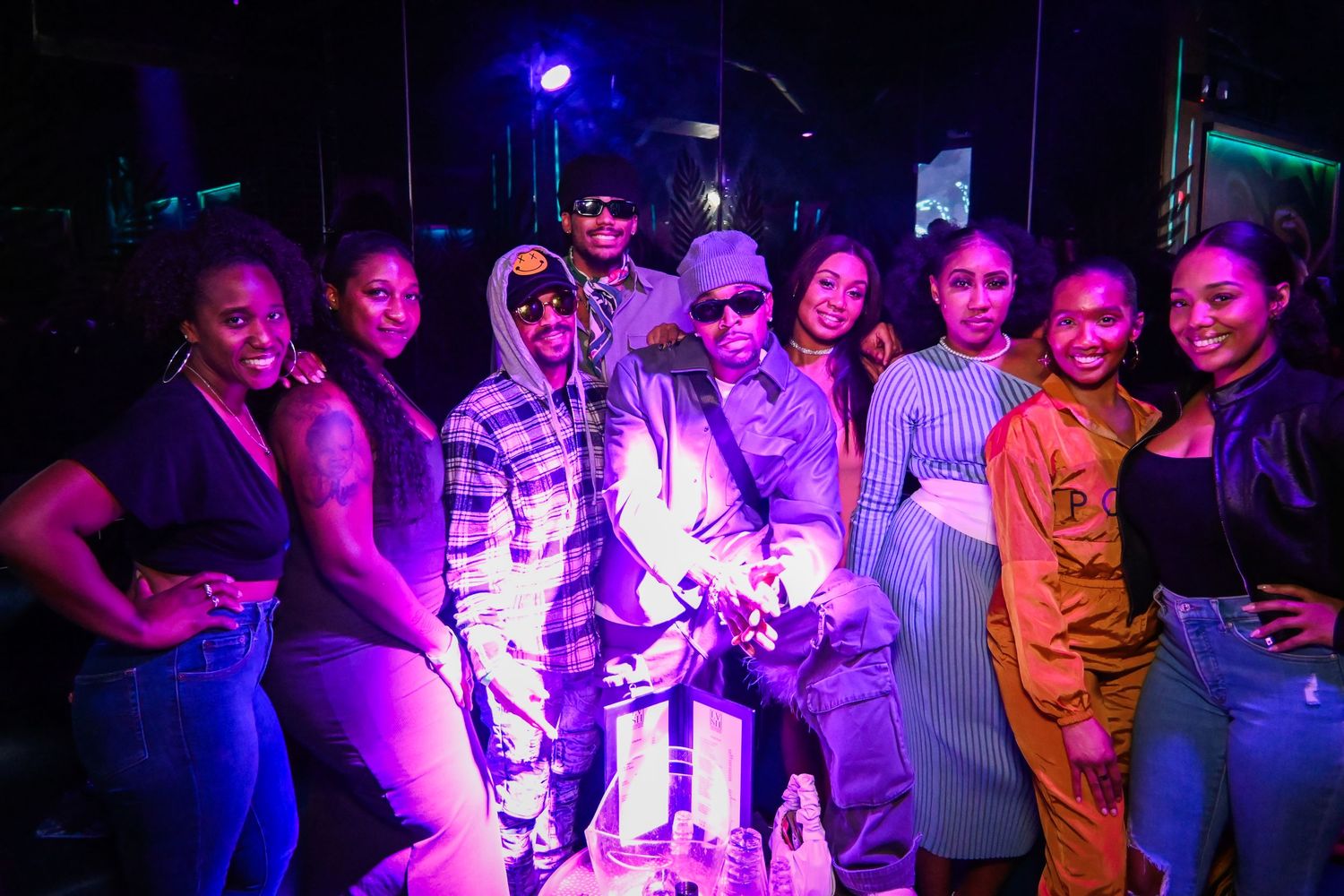 People enjoying a nightclub atmosphere with purple and blue lighting while dancing and socializing on the dance floor.