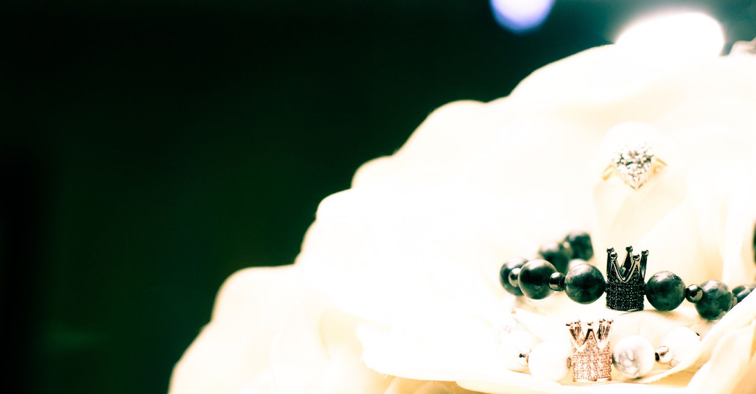 Close-up of elegant jewelry pieces including a beaded bracelet with crown charm displayed on a white floral surface.