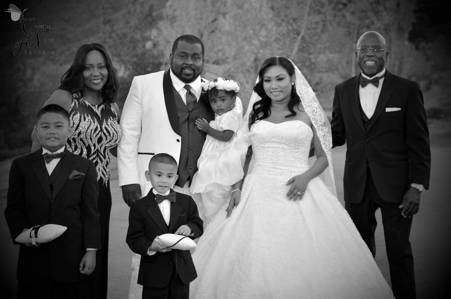 Black and white wedding photo of a couple in formal attire surrounded by family members including children in tuxedos.