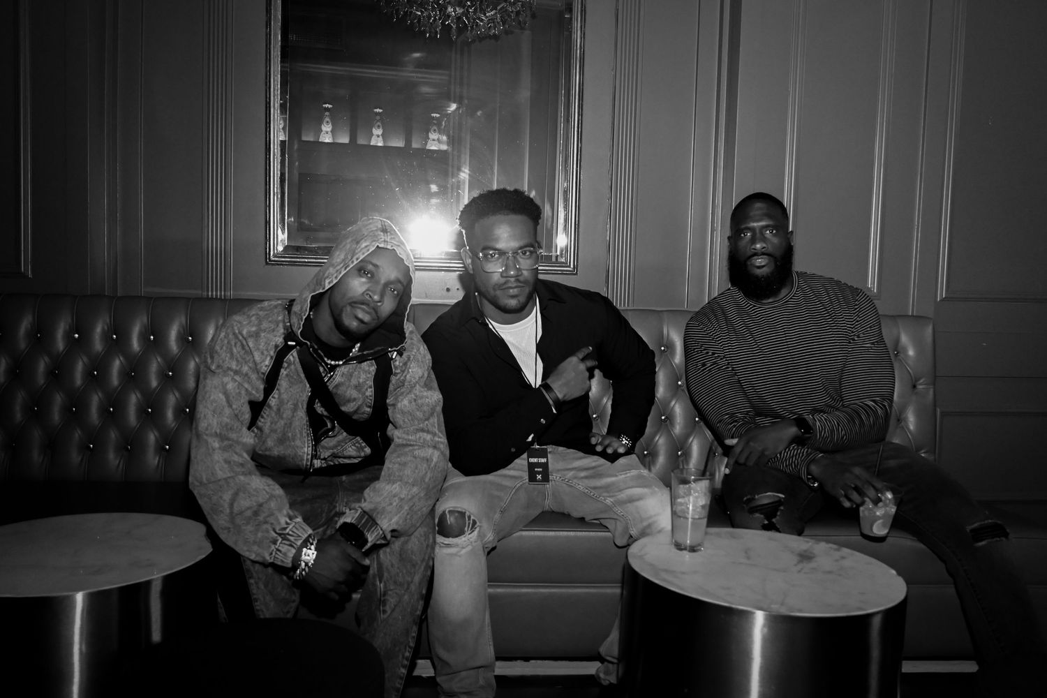 Three people sitting together on a couch at a lounge, relaxing with drinks in a black and white photograph.