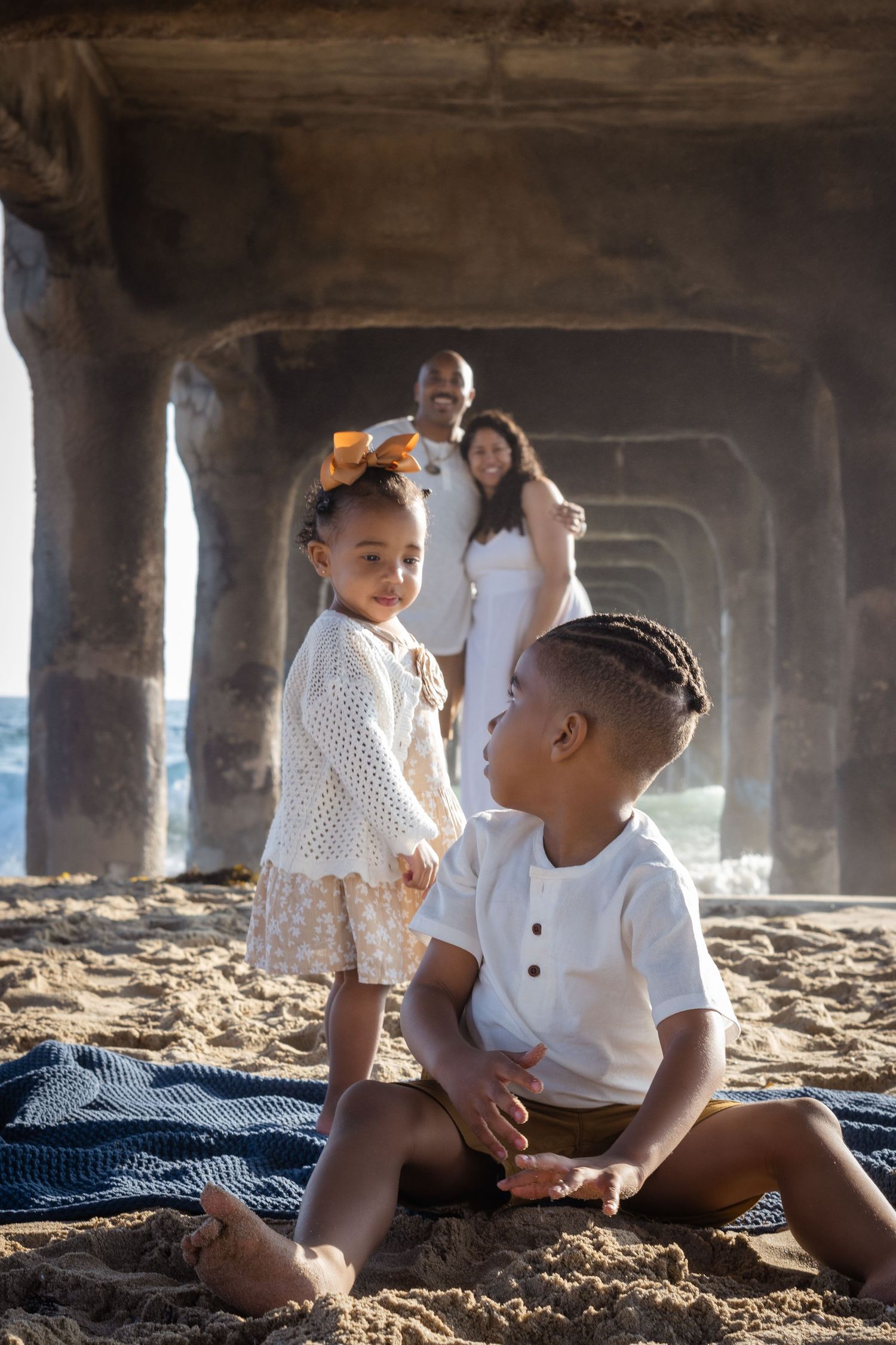 Family enjoying a peaceful moment together on a sandy beach under a pier on a sunny day.