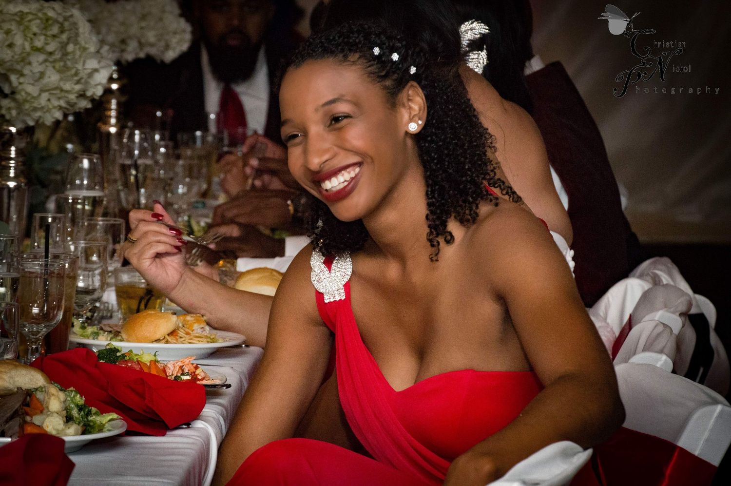 Woman in red dress smiling at a formal dinner table with food and drinks at an elegant event.