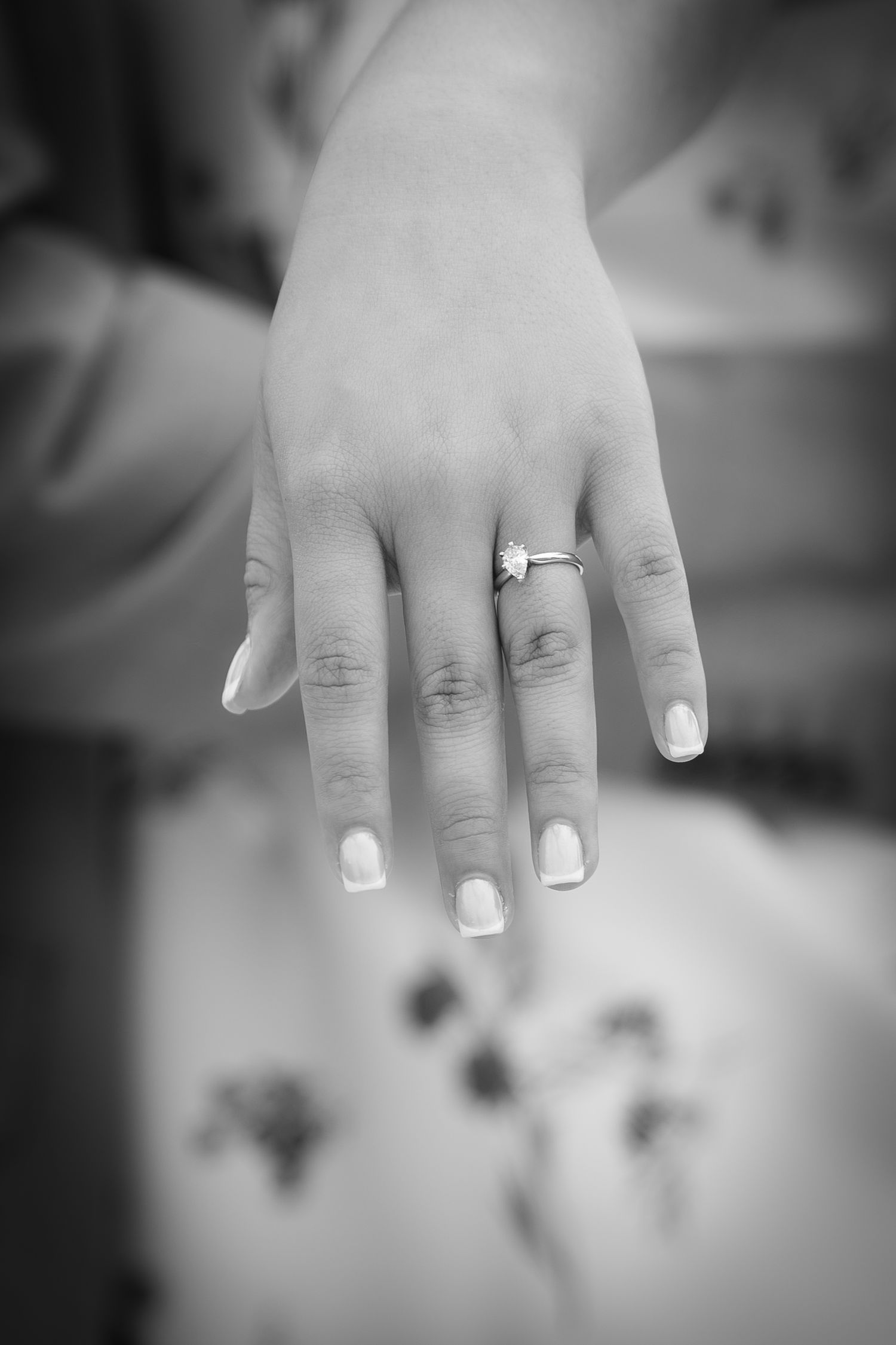 Black and white photo of a woman's hand displaying a diamond engagement ring on her ring finger.