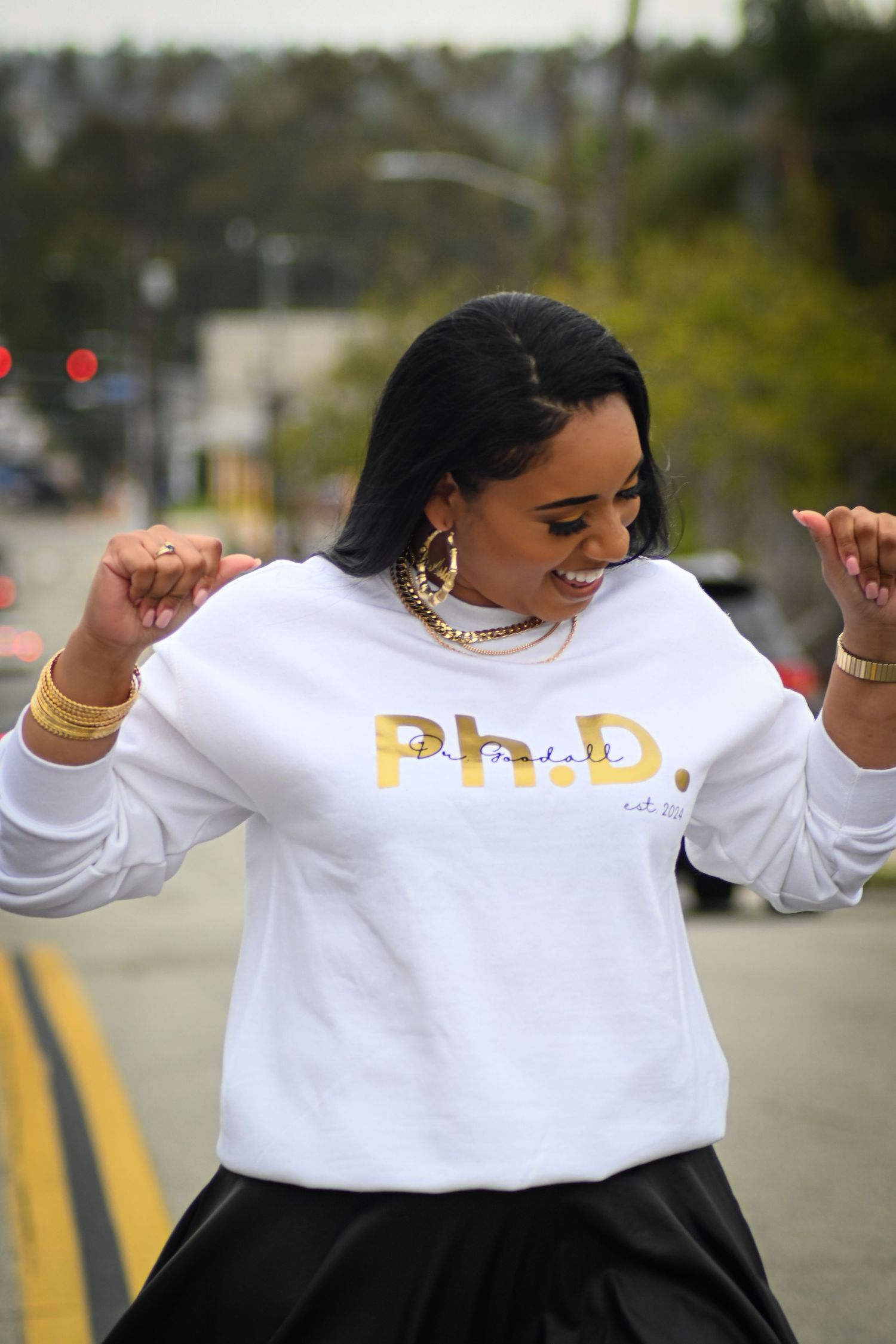 Energetic dance pose in a white sweatshirt with gold text on a city street.