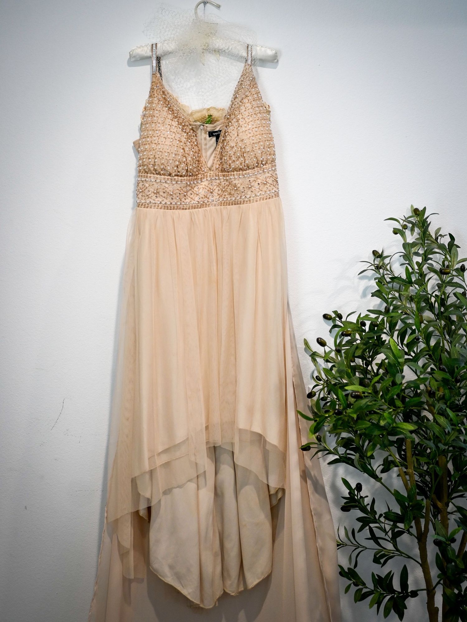 Elegant blush pink high-low formal gown with beaded bodice and flowing tulle skirt on hanger.