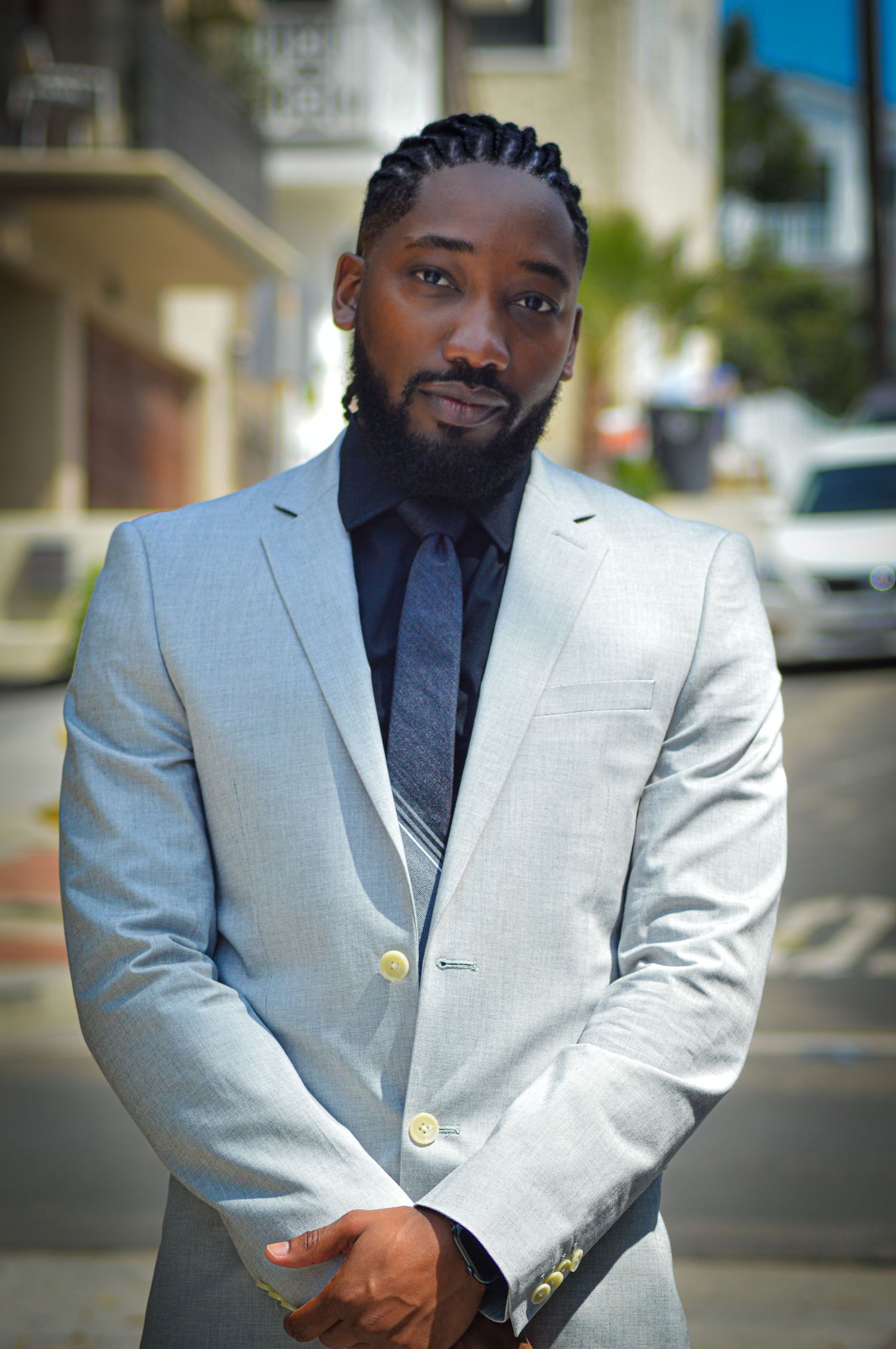 A person in a light gray blazer and navy shirt poses outdoors in a professional photoshoot series.