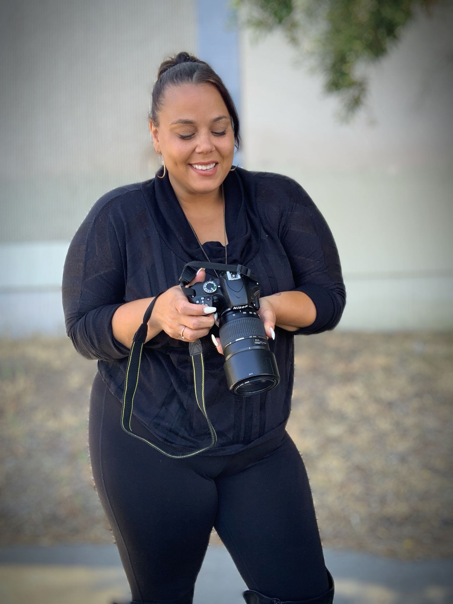 Photographer in all black outfit crouching with camera in outdoor setting.