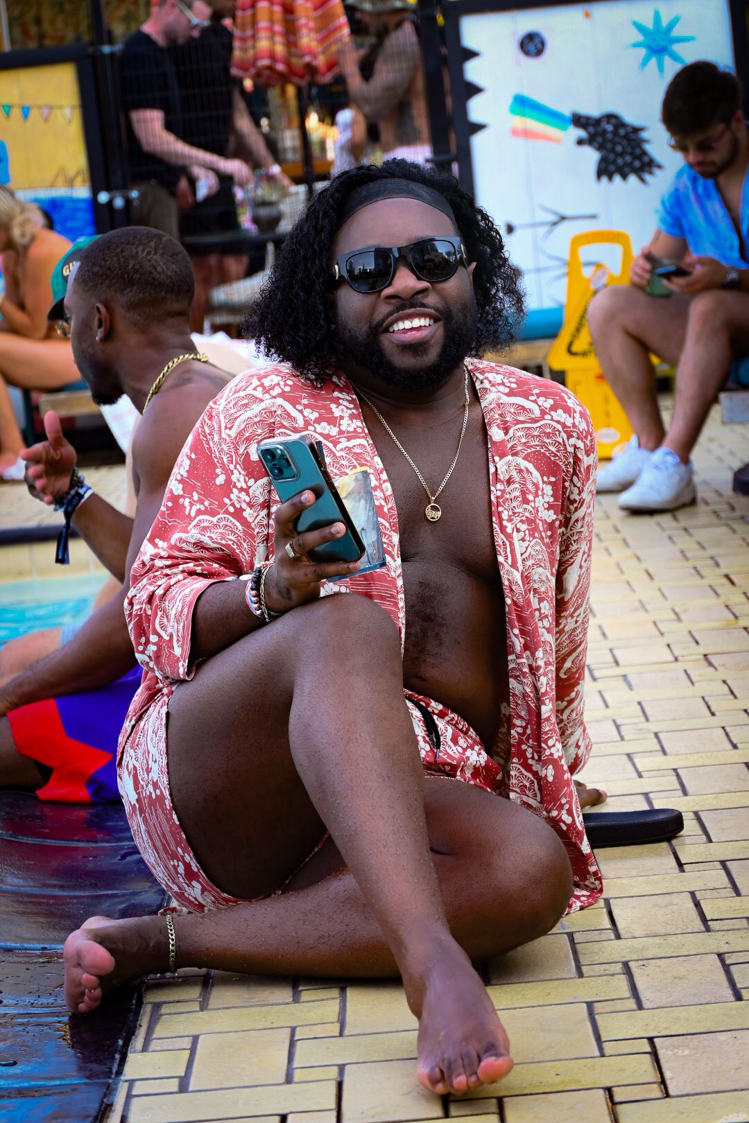 A person in a red and white patterned shirt relaxes on a tiled floor during what appears to be a festive gathering.