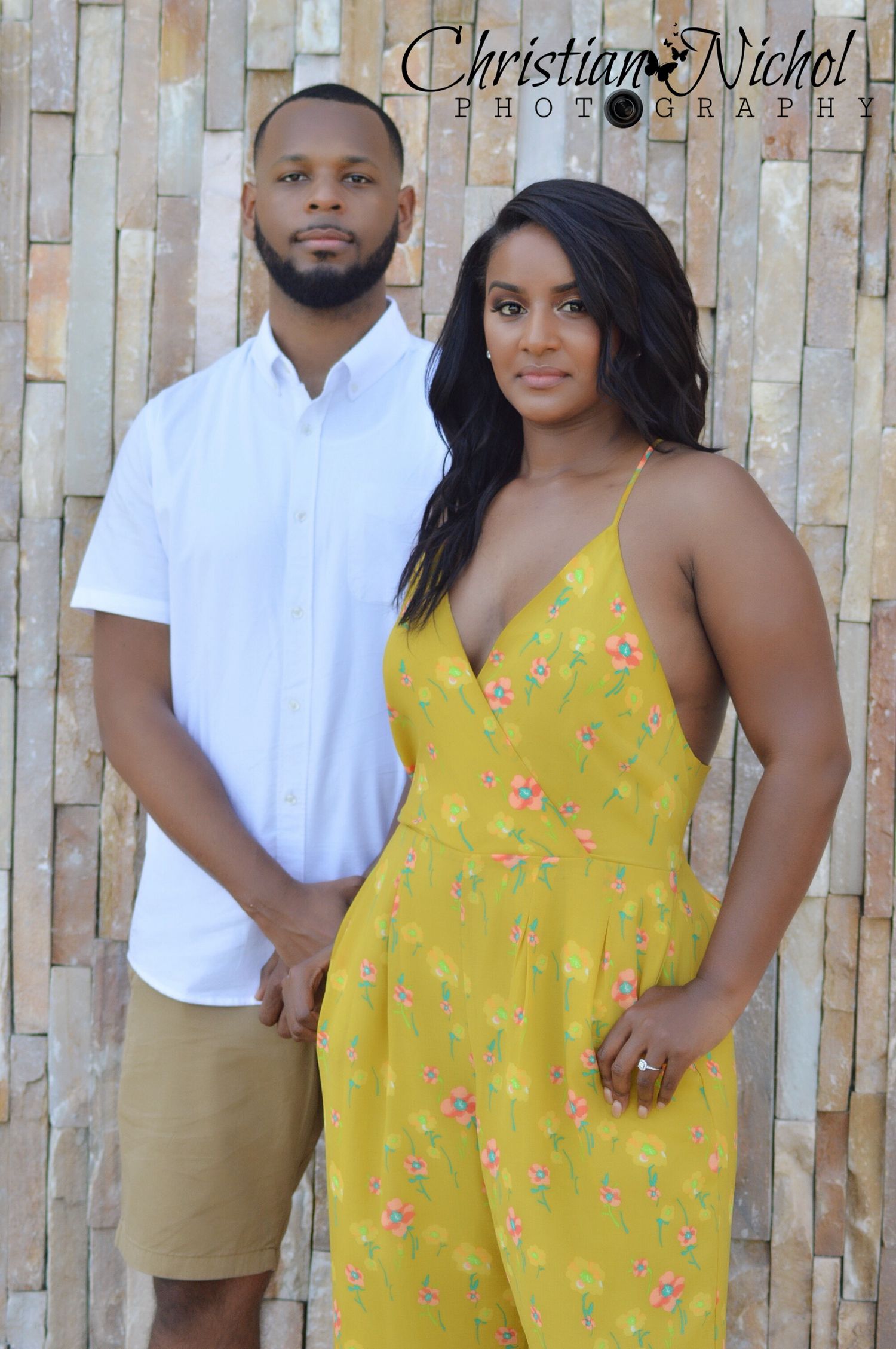 A couple poses together, woman in yellow floral jumpsuit and man in white shirt, photographed by Christian Nichol Photography.