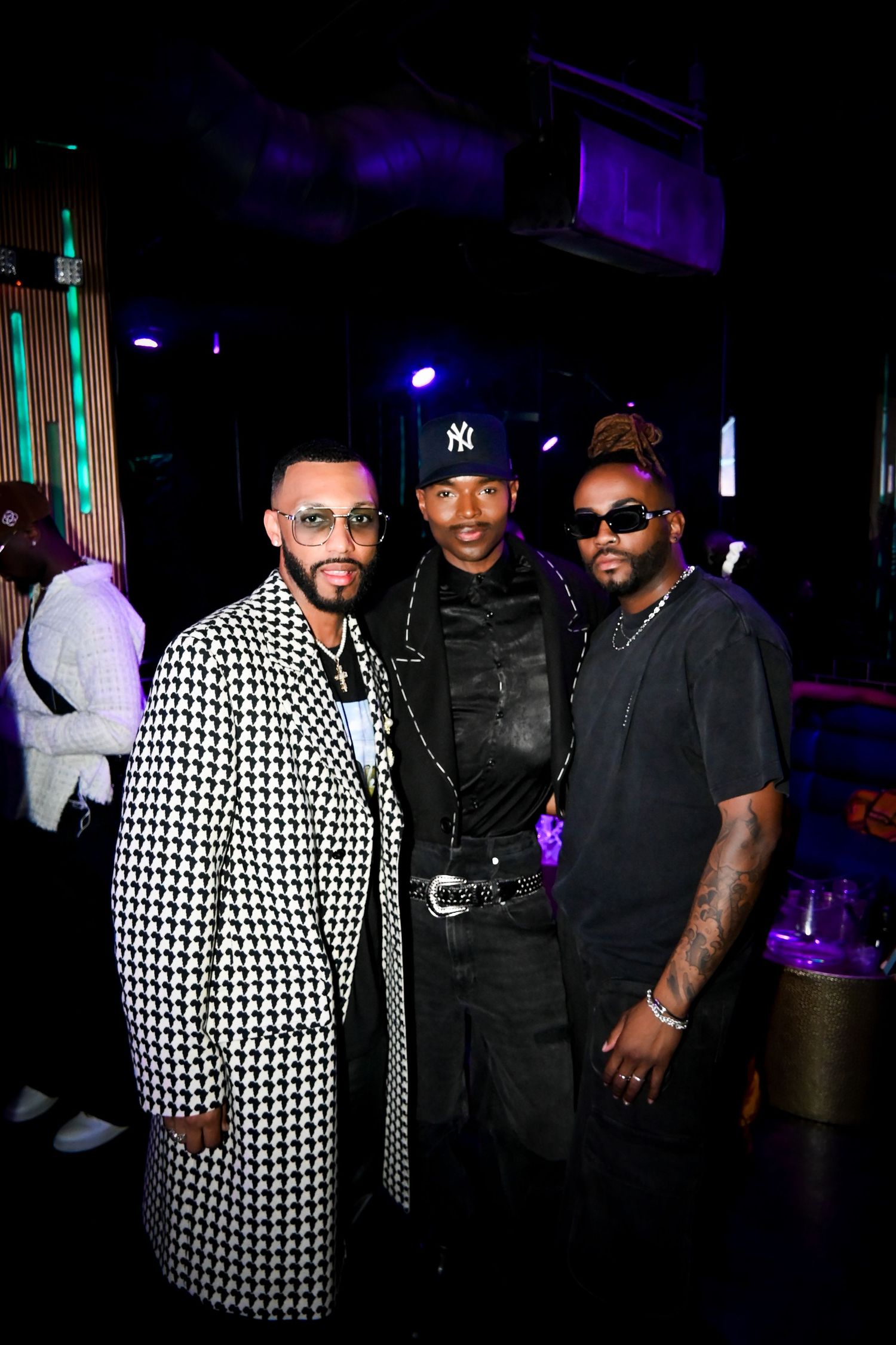 Group of performers posing together at a nightclub wearing black and patterned outfits in dark lighting.