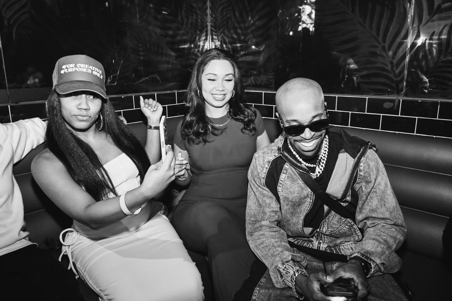 Black and white nightclub photo showing three people seated together in a booth smiling and posing for the camera.