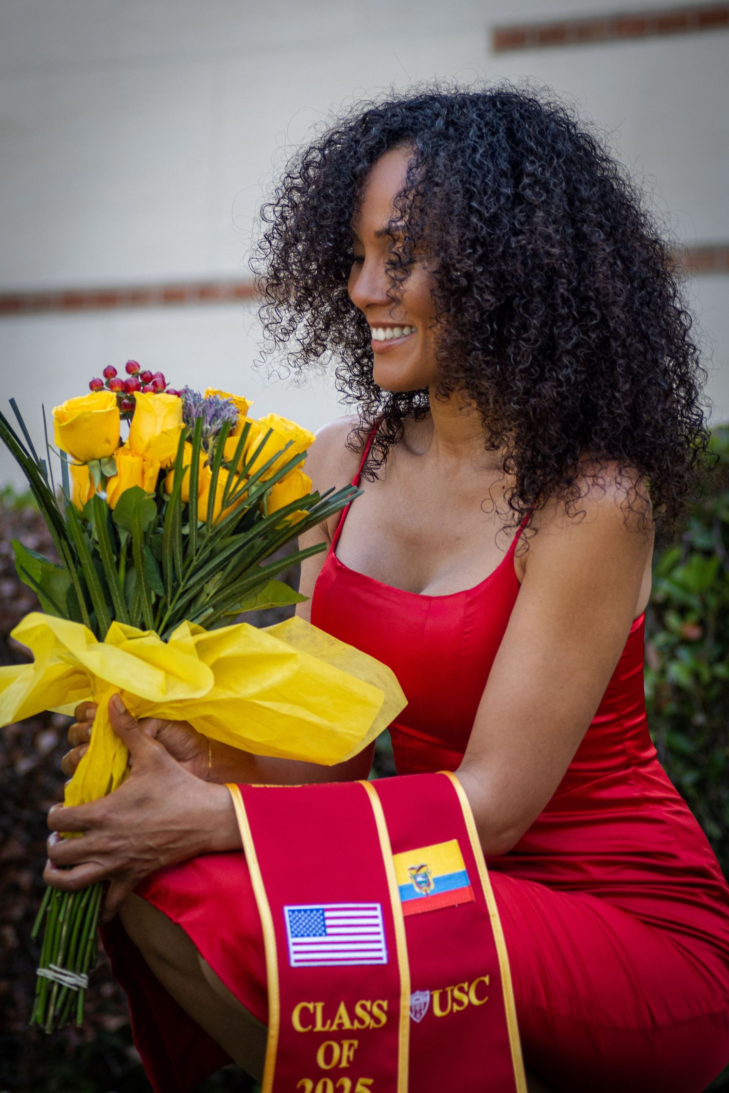 Graduate in red dress poses with sunflowers and USC graduation stole outdoors.