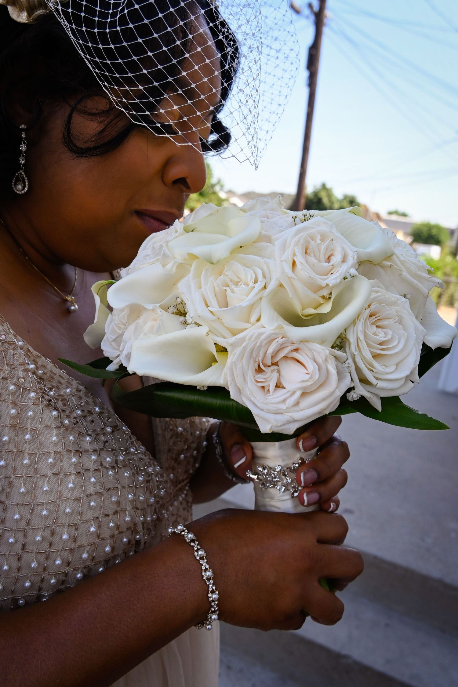 Bride in beaded gown and birdcage veil holds white rose and calla lily wedding bouquet wrapped in pearl ribbon.