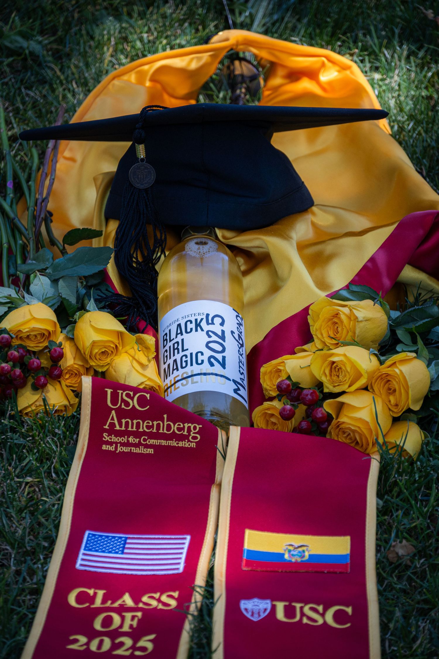Graduation cap and USC stoles displayed with yellow roses and diploma holder.