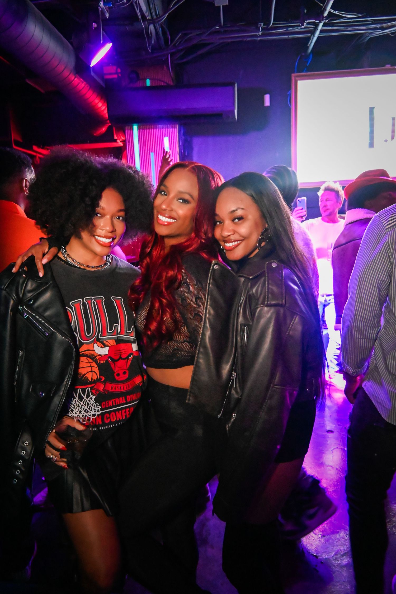 Friends enjoying a night out at a club with purple and pink lighting in the background.