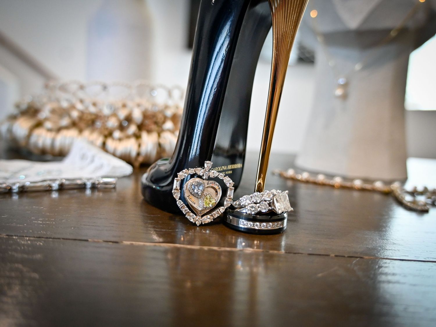 Close-up of elegant diamond wedding rings and heart-shaped brooch beside black high heel shoes on wooden floor.