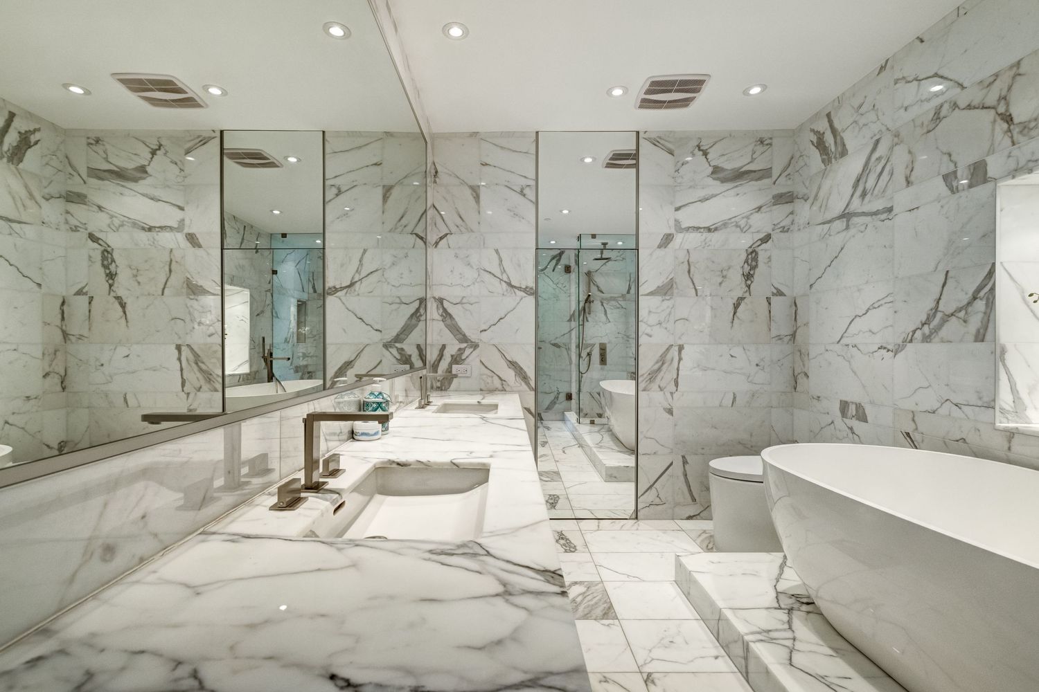 Luxurious marble bathroom with freestanding soaking tub, glass shower, and floor-to-ceiling white Calacatta marble walls.