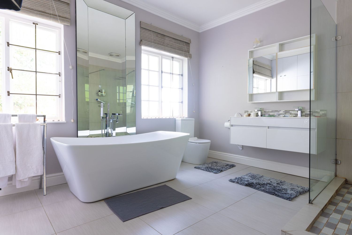 Modern luxury bathroom with freestanding soaking tub, glass shower, floating vanity, and large windows with natural light.