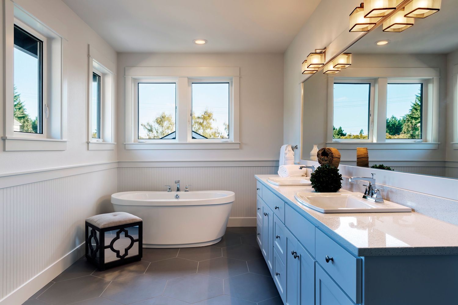 Modern bathroom with freestanding soaking tub, blue vanity, dual sinks, and bright natural light.