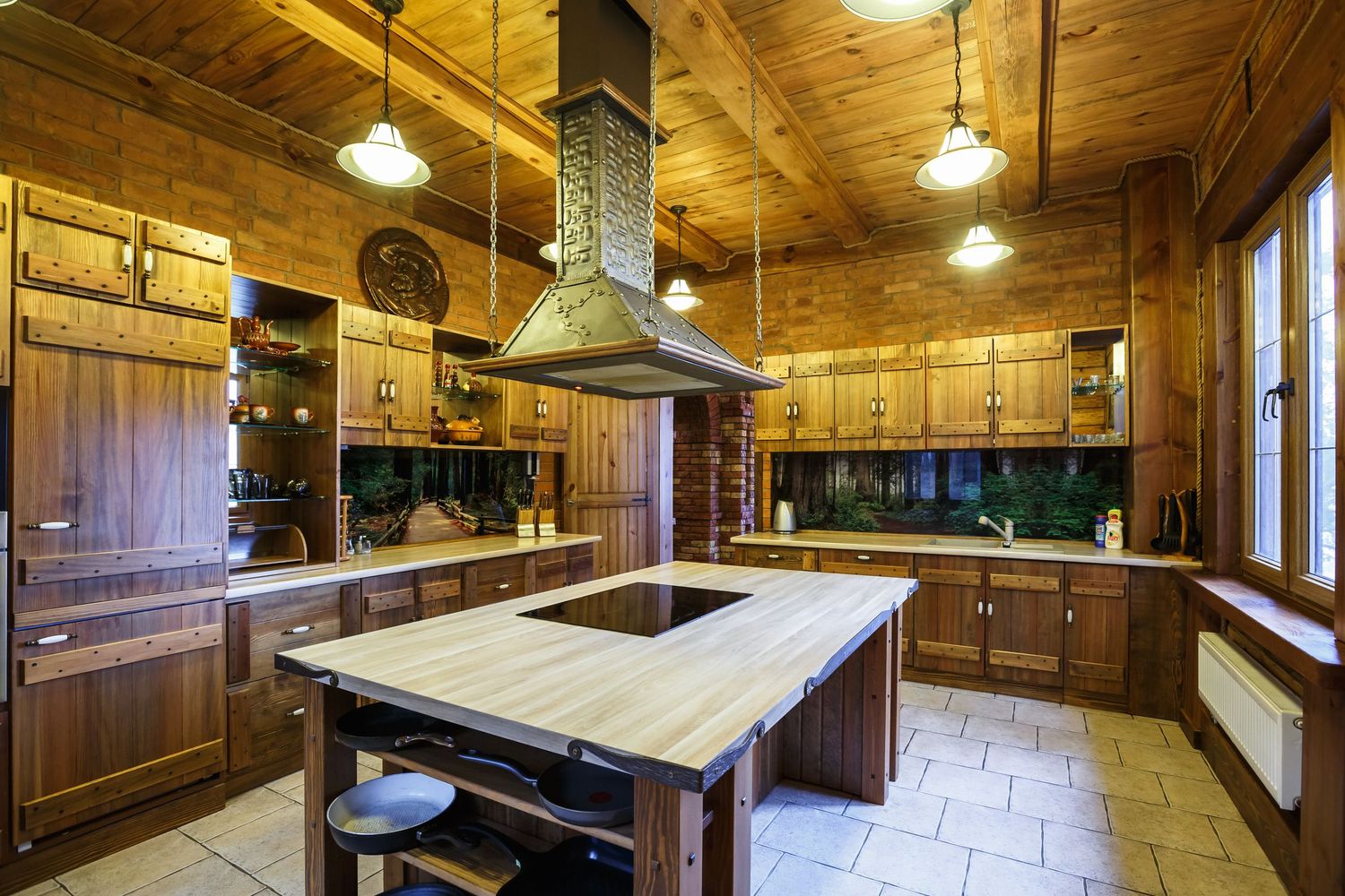 Rustic wooden kitchen with large island, butcher block countertop, range hood, pendant lights, and warm cabinetry throughout.