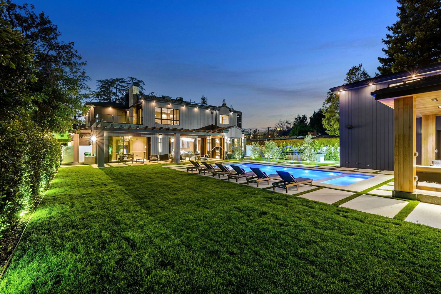 Stunning luxury estate with expansive lawn, pool, and lounge chairs beautifully lit at twilight.