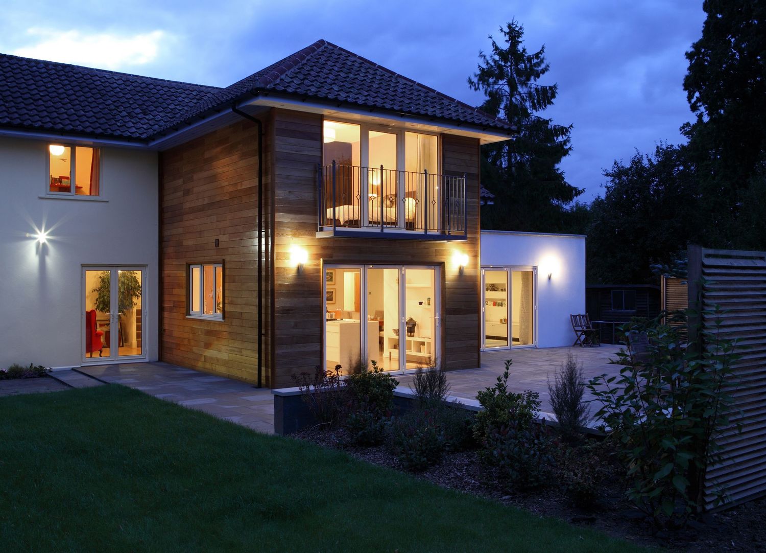 Contemporary two-story home with wood cladding and large windows illuminated at dusk.