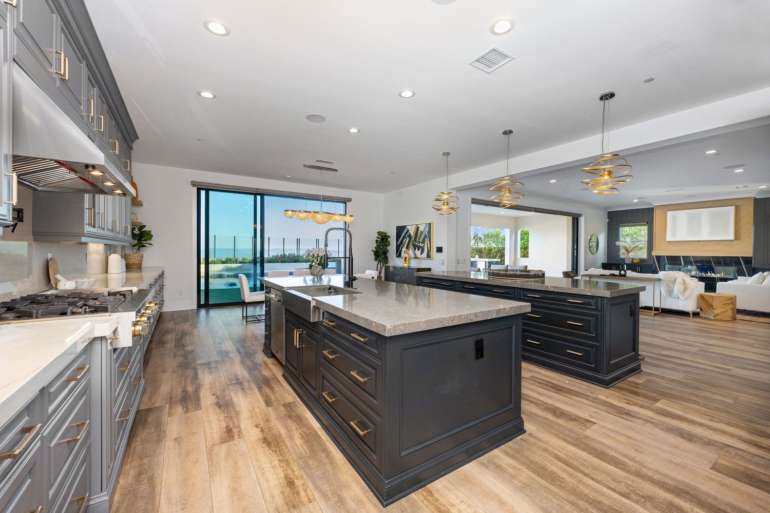Spacious open-concept kitchen with dark gray island, quartz countertops, hardwood floors, and pendant lights overlooking living area.