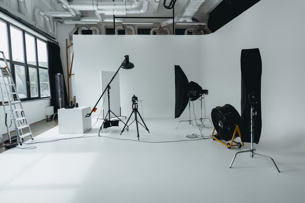 Professional photography studio with white backdrop, lighting equipment, softboxes, and camera on tripod setup.