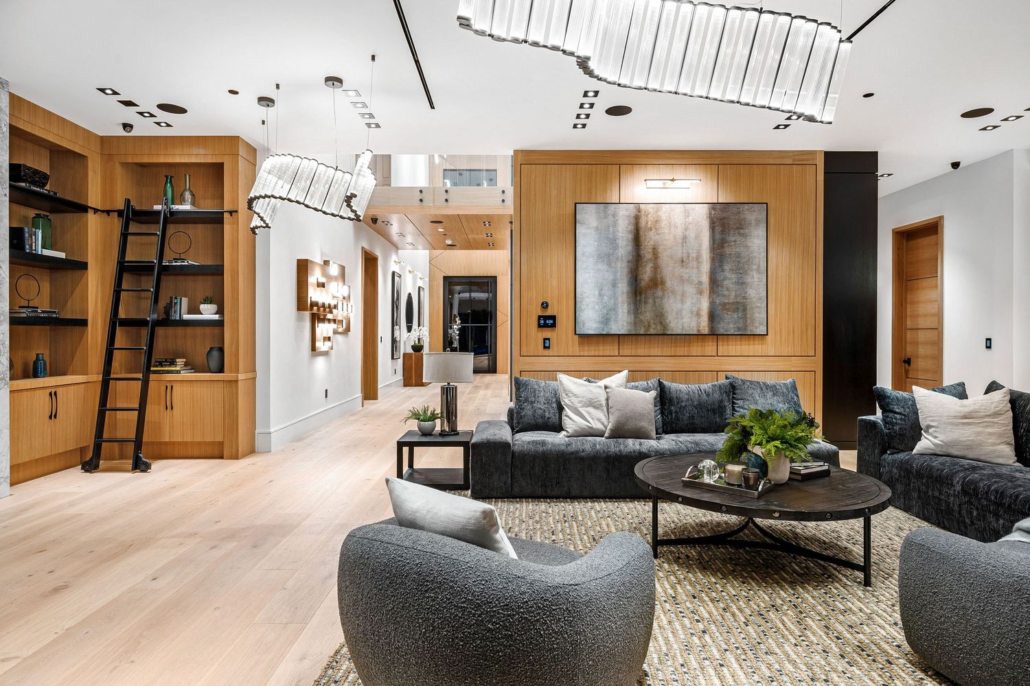 Modern living room with gray sofas, wood-paneled walls, built-in shelving, rolling ladder, and abstract art.