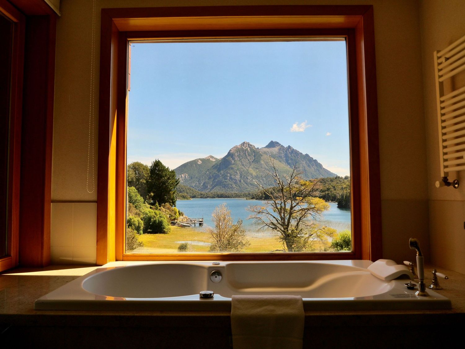 Luxurious bathtub with a stunning window view of a mountain lake and lush green trees in a serene retreat.