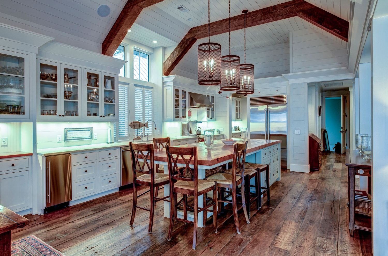 Rustic kitchen with hardwood floors, white cabinets, wooden beam ceiling, and hanging lantern pendant lights over island.