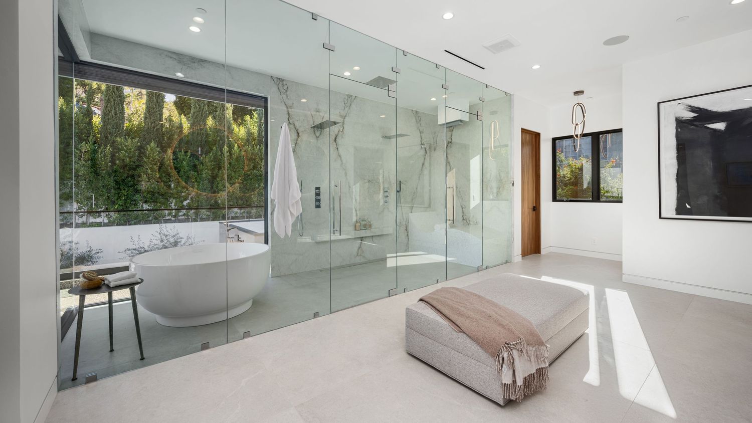 Luxurious modern bathroom with glass-enclosed shower, freestanding soaking tub, and floor-to-ceiling windows overlooking lush greenery.