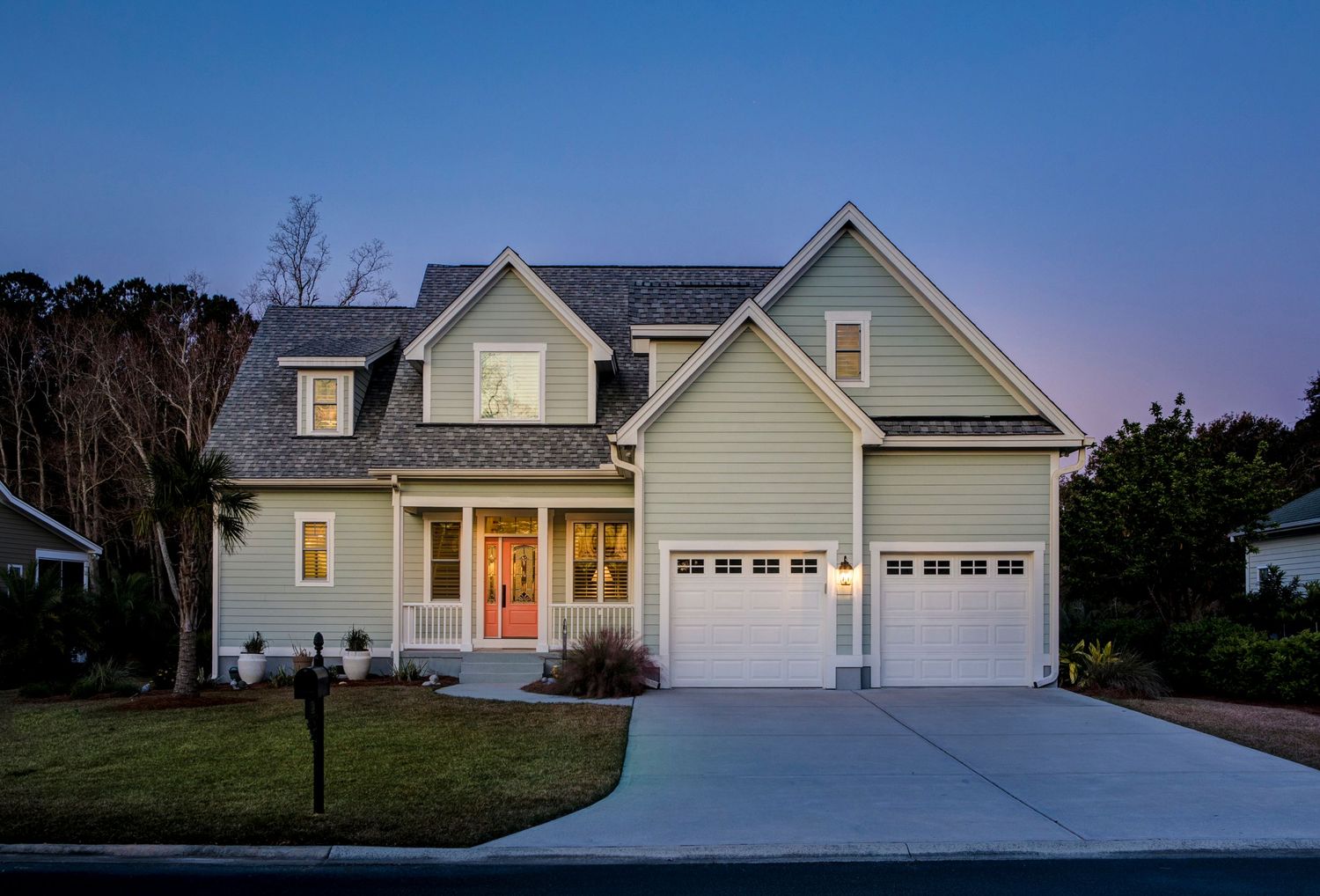 Charming two-story craftsman home with gray siding, red front door, and two-car garage photographed at dusk.